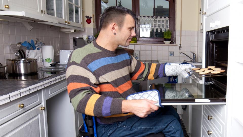 Mann im Rollstuhl holt Kekse aus dem Backofen